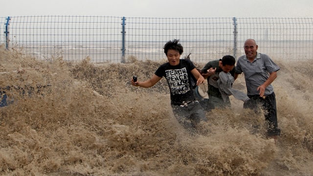 Drei Männer werden auf einer Strasse von einer Welle überrascht. Drei Männer werden auf einer Strasse von einer Welle überrascht.