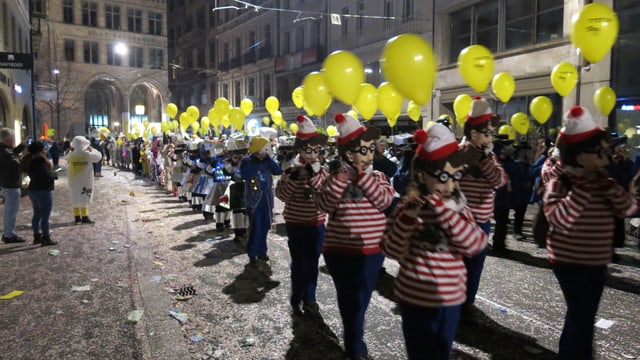 Piccolo-Spieler mit gelben Ballonen ziehen in Formation durch eine Strasse. Piccolo-Spieler mit gelben Ballonen ziehen in Formation durch eine Strasse.