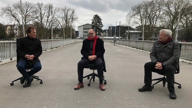 Drei Herren sitzen auf Bürostühlen auf der Kreuzackerbrücke in Solothurn und reden miteinander. Drei Herren sitzen auf Bürostühlen auf der Kreuzackerbrücke in Solothurn und reden miteinander.