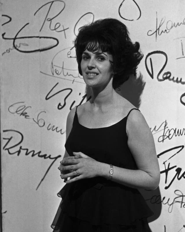Die Sängerin Wanda Jackson steht vor einer mit vielen Schriftzügen dekorierten Wand. Die Sängerin Wanda Jackson steht vor einer mit vielen Schriftzügen dekorierten Wand.
