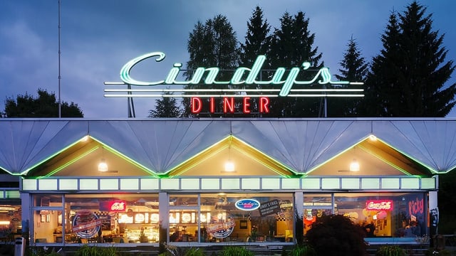 Eine Autobahnrestaurant in der Nacht, darüber steht in Neonschrift «Cindy's Diner». Eine Autobahnrestaurant in der Nacht, darüber steht in Neonschrift «Cindy's Diner».