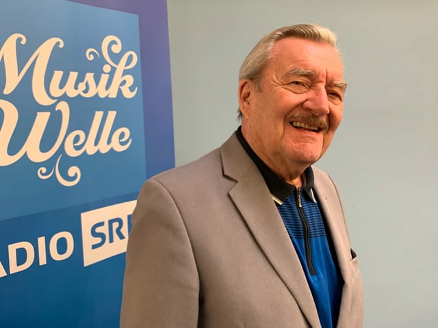 Mann im Anzug vor Musikwelle-Logo. Mann im Anzug vor Musikwelle-Logo.