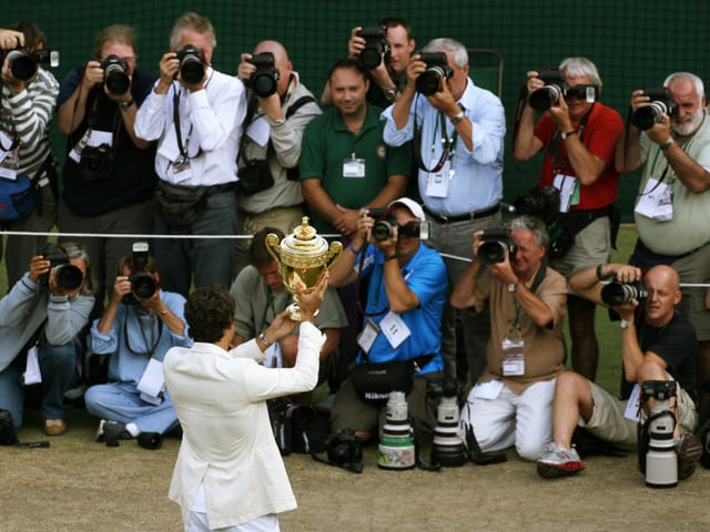 Rückenansicht von Federer, wie er den Fotografen den Pokal entgegenstemmt.