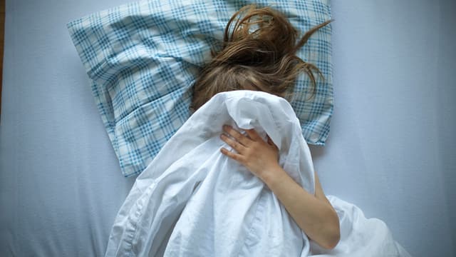 Mädchen liegt im Bett und zieht die Bettdecke über den Kopf. Mädchen liegt im Bett und zieht die Bettdecke über den Kopf.