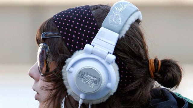 Eine junge Frau mit Sonnenbrille trägt einen grossen, silbernen Kopfhörer. Eine junge Frau mit Sonnenbrille trägt einen grossen, silbernen Kopfhörer.