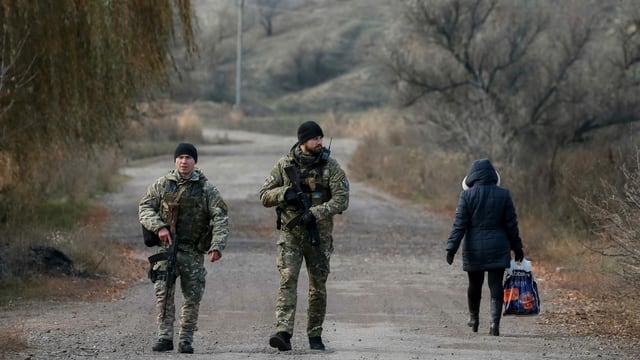 Soldaten patrrouillieren auf einer Strasse im Donbass, eine Zivilistin geht vorbei. Soldaten patrrouillieren auf einer Strasse im Donbass, eine Zivilistin geht vorbei.