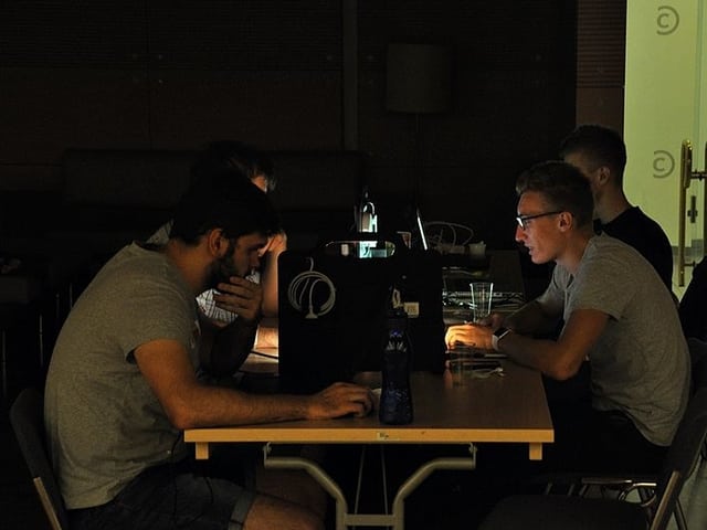 Gruppe junger Männder im Halbdunkel an einem Tisch mit verschiedenen Computern. Gruppe junger Männder im Halbdunkel an einem Tisch mit verschiedenen Computern.