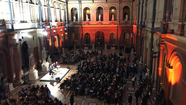 Podium mit mehreren Menschen in einem grossen Saal Podium mit mehreren Menschen in einem grossen Saal