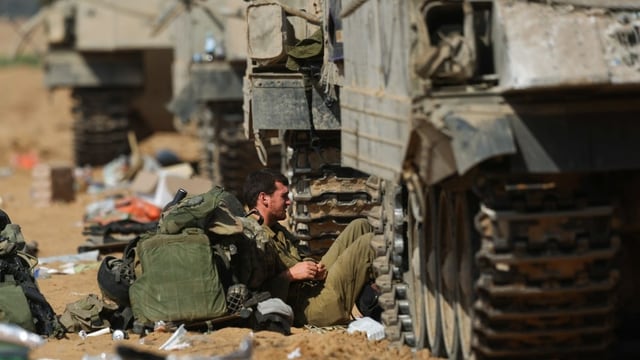 Soldat sitzt neben Militärfahrzeugen am Boden und ruht sich aus. Soldat sitzt neben Militärfahrzeugen am Boden und ruht sich aus.