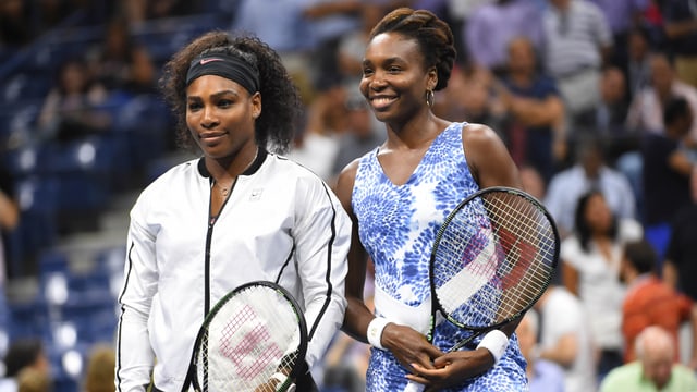 Serena und Venus Williams lächeln am Netz in die Kameras. Serena und Venus Williams lächeln am Netz in die Kameras.