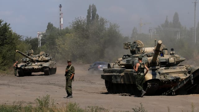 Zwei Panzer stehen auf einer Strasse, daneben zwei Soldaten Zwei Panzer stehen auf einer Strasse, daneben zwei Soldaten