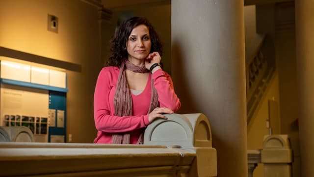 Dunkles Haar, pinker Pullover: Eine junge Frau in Denkerpose steht neben einer Säule. Dunkles Haar, pinker Pullover: Eine junge Frau in Denkerpose steht neben einer Säule.