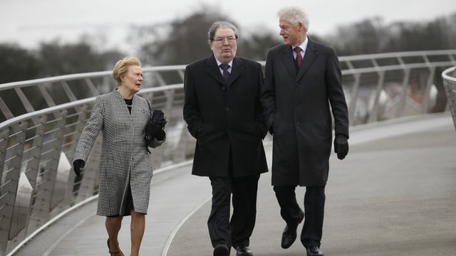 Drei Personen in festlicher Kleidung gehen über eine Brücke Drei Personen in festlicher Kleidung gehen über eine Brücke