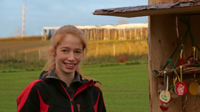 Eine Frau mit roten Haaren, die sie zum Rossschwanz zusammengebunden hat, steht vor einer Weide. Eine Frau mit roten Haaren, die sie zum Rossschwanz zusammengebunden hat, steht vor einer Weide.