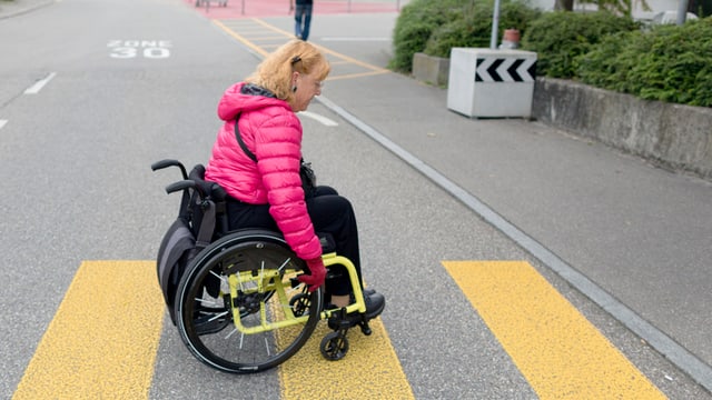 Frau im Rollstuhl überquert Strasse Frau im Rollstuhl überquert Strasse