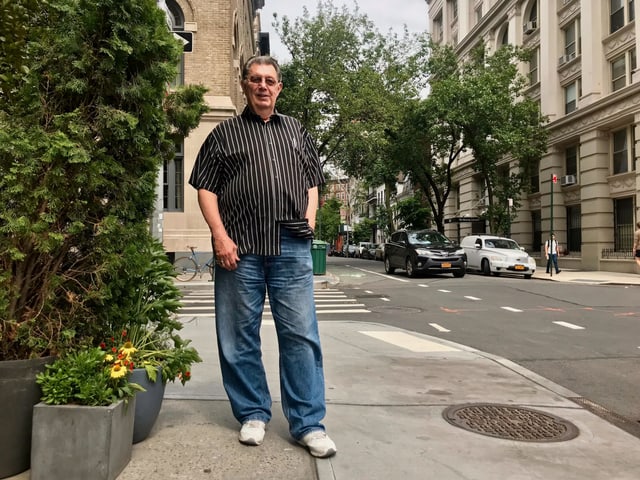 Ein Mann steht auf dem Troittoir in einer Grosstadt. Hinter ihm eine leere Strassenkreuzung mit Fussgängerstreifen. Ein Mann steht auf dem Troittoir in einer Grosstadt. Hinter ihm eine leere Strassenkreuzung mit Fussgängerstreifen.