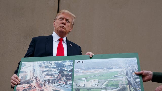Donald Trump hält ein Plakat und schaut sehr entschlossen