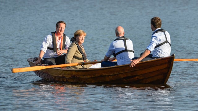 Cameron, Merkel, der schwedische Premier Fredrik Reinfeldt und sein dänischer Amtskollege Mark Rutte sitzen mit Schwimmwesten in einem Ruderboot auf einem See.
