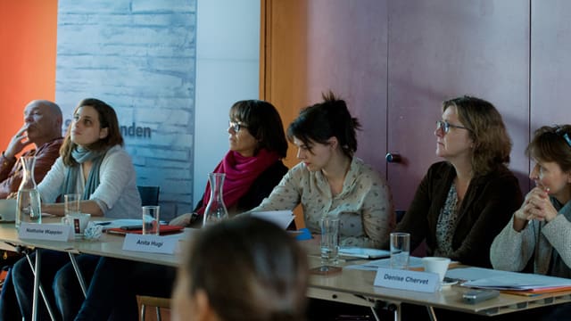 Die Jury, bestehend aus 6 Personen, an einem langen Tisch sitzend, zuhörend, Notizen machend. Die Jury, bestehend aus 6 Personen, an einem langen Tisch sitzend, zuhörend, Notizen machend.