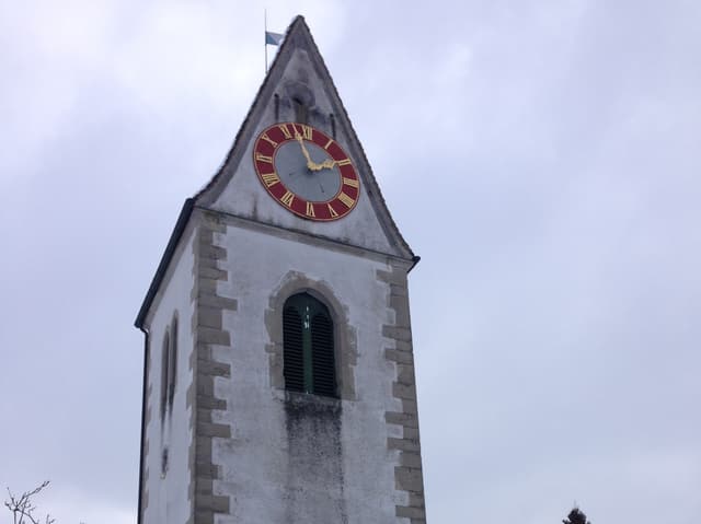 Ein weisser Kirchturm mit rotem Zifferblatt