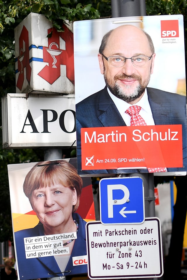 Placats dad Angela Merkel e Martin Schulz vid in pitga cun tavla da parcar ed inscripziuns. Placats dad Angela Merkel e Martin Schulz vid in pitga cun tavla da parcar ed inscripziuns.