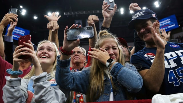 Fans von Donald Trump halten Handys hoch, eine junge Frau wischt sich Tränen ab. Fans von Donald Trump halten Handys hoch, eine junge Frau wischt sich Tränen ab.