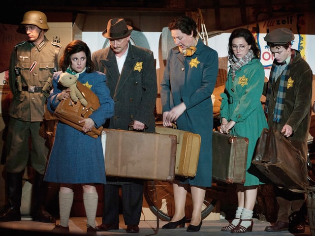 Anne Frank trägt eine Tasche und einen Teddy und wartet zusammen mit anderen Juden. Anne Frank trägt eine Tasche und einen Teddy und wartet zusammen mit anderen Juden.