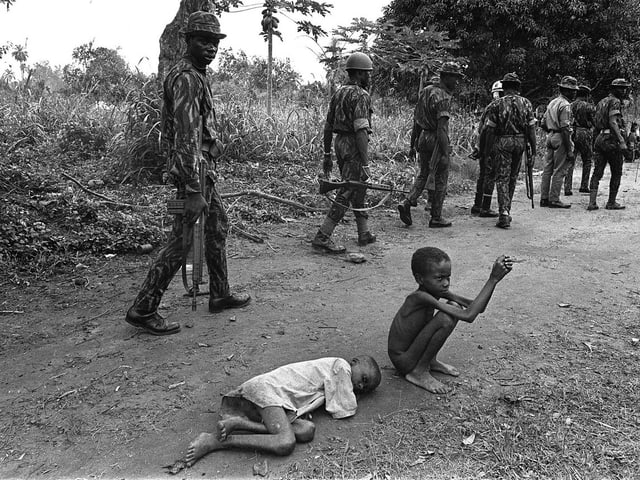 Soldaten der nigerianischen Bundesarmee gehen an zwei abgemagerten Kindern vorbei. Soldaten der nigerianischen Bundesarmee gehen an zwei abgemagerten Kindern vorbei.