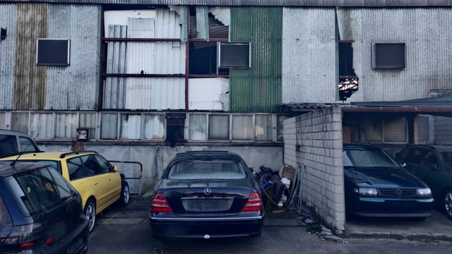 Wellblech-Halle mit Löchern in Wänden, davor alte Autos. Wellblech-Halle mit Löchern in Wänden, davor alte Autos.