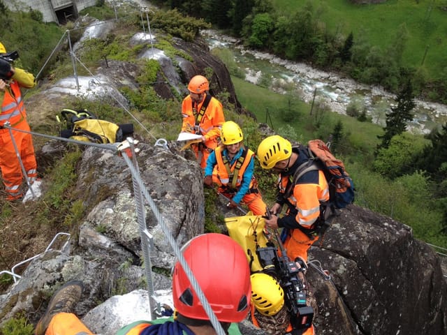Fünf Personen hängen an starken Seilen in den Felsen und werden dabei gefilmt.