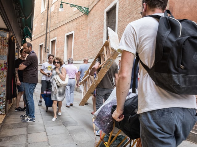 Ein mann mit einer Bauleiter geht an Touristen vorbei durch eine schmale Gasse. Ein mann mit einer Bauleiter geht an Touristen vorbei durch eine schmale Gasse.