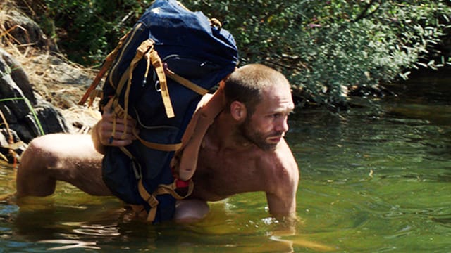 Mann in Unterwäsche lauert im Wasser und hält einen Rucksack über Wasser. Mann in Unterwäsche lauert im Wasser und hält einen Rucksack über Wasser.