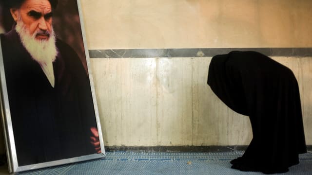 Frau mit Tschador vor Bild von Chomeini. Frau mit Tschador vor Bild von Chomeini.