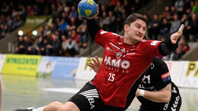 Ein Mann in einem roten Trikot wirft ein Handball. Ein Mann in einem roten Trikot wirft ein Handball.