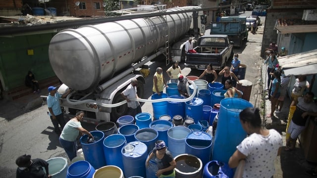 Einwohner von Caracas füllen Trinkwasser aus einem Tanklaster in grosse blaue Fässer. Einwohner von Caracas füllen Trinkwasser aus einem Tanklaster in grosse blaue Fässer.
