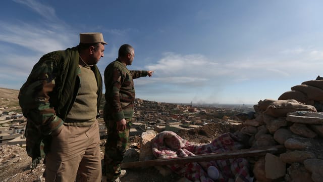 Ein Mann zeigt auf eine Gemeinde im Hintergrund, ein anderer schaut dorthin Ein Mann zeigt auf eine Gemeinde im Hintergrund, ein anderer schaut dorthin
