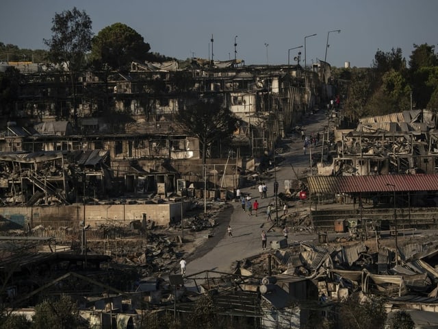 Ein Mann geht &uuml;ber die Tr&uuml;mmer des Fl&uuml;chtlingscamps hinweg durch den Rauch.