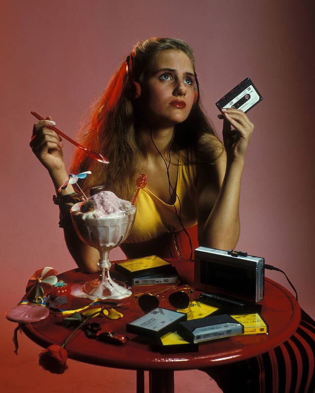 Eine Frau löffelt ein Eis und hält in der anderen Hand eine Kassette. Eine Frau löffelt ein Eis und hält in der anderen Hand eine Kassette.