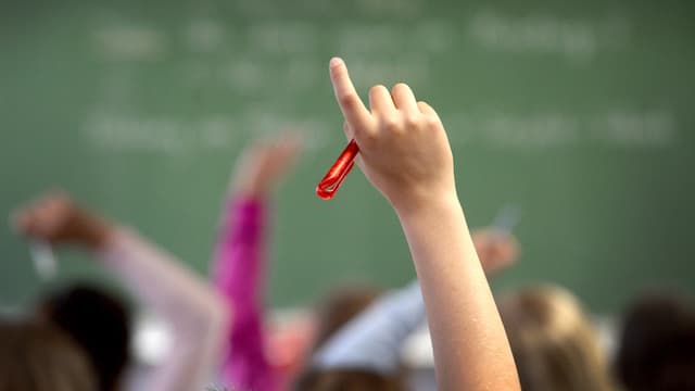Symbolbild: In einem Schulzimmer sieht man aufgestreckte Hände, im Hintergrund eine Wandtafel. Symbolbild: In einem Schulzimmer sieht man aufgestreckte Hände, im Hintergrund eine Wandtafel.