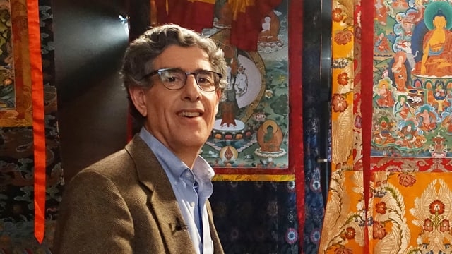 Mann mit Brille vor bunten Wandteppichen Mann mit Brille vor bunten Wandteppichen