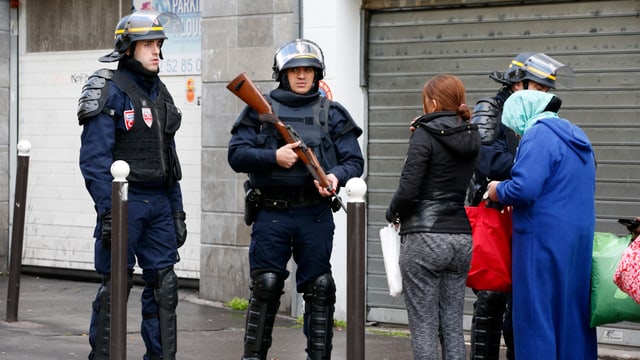 Bewaffnete Polizisten kontrollieren zwei Passantinnen. Bewaffnete Polizisten kontrollieren zwei Passantinnen.