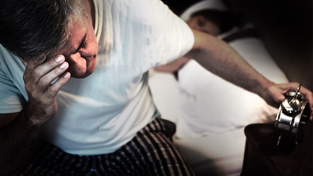 Mann sitzt auf Bettkante und schaut verzweifelt auf den Wecker. Mann sitzt auf Bettkante und schaut verzweifelt auf den Wecker.