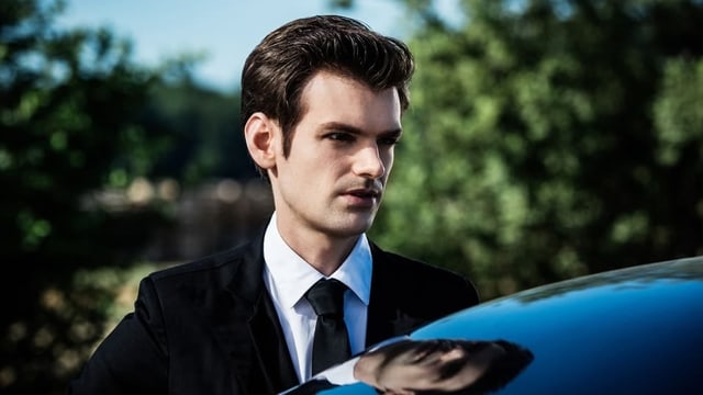 Ein Mann steht hinter einem Auto. Man sieht nur Kopf und Schultern. Er schaut ernst. Ein Mann steht hinter einem Auto. Man sieht nur Kopf und Schultern. Er schaut ernst.