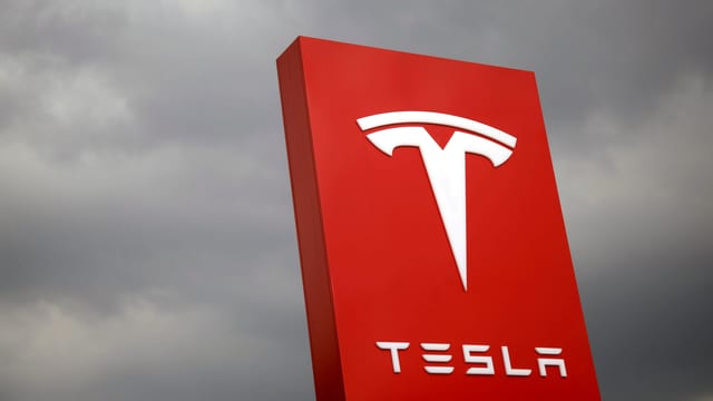 Das Tesla-Logo vor grauen Wolken Das Tesla-Logo vor grauen Wolken