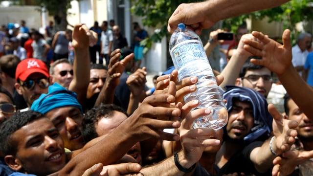 Flüchtlinge strecken ihre Hände nach einer Wasserflasche aus Flüchtlinge strecken ihre Hände nach einer Wasserflasche aus