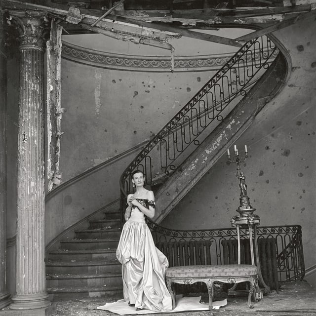 Eine Frau steht am Ende einer schönen, steinernen Treppe. Sie trägt ein schulterfreies, opulentes Kleid.