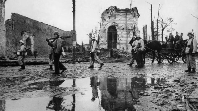 Eine verregnete, schlammige Strasse. Im Hintergrund ein zerbomtes Gebäude. Vereinzelte Soldaten und en Pferdewagen gehen der Strasse entlang. Eine verregnete, schlammige Strasse. Im Hintergrund ein zerbomtes Gebäude. Vereinzelte Soldaten und en Pferdewagen gehen der Strasse entlang.