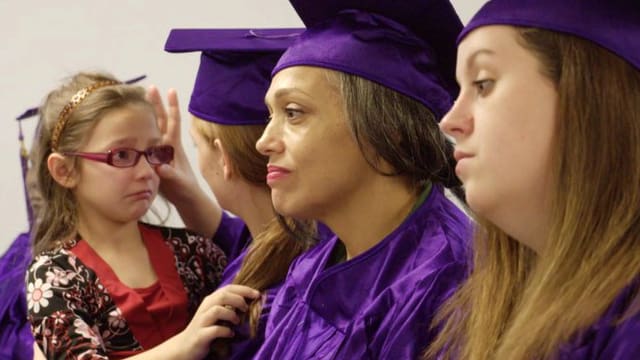 rauen in violetten Abschlussroben, eine hat ein weinendes Kind auf dem Arm. rauen in violetten Abschlussroben, eine hat ein weinendes Kind auf dem Arm.