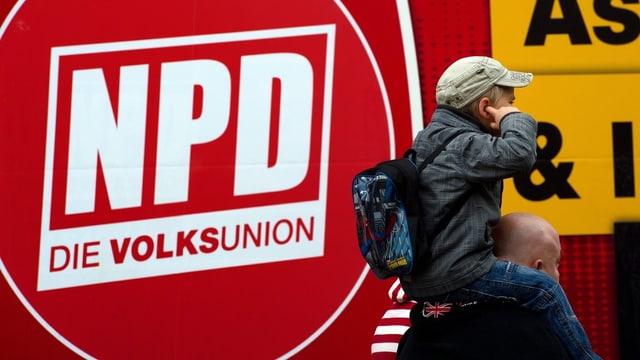 Ein rotes NPD Plakat. Davor hält sich ein kleiner Bube die Ohren zu Ein rotes NPD Plakat. Davor hält sich ein kleiner Bube die Ohren zu