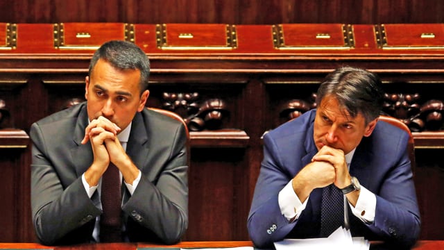 Di Maio und Conte sitzen im Parlament, das Kinn in die Hände gestützt und hören zu. Di Maio und Conte sitzen im Parlament, das Kinn in die Hände gestützt und hören zu.